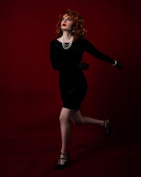 Stylish portrait of a woman in a black dress posing gracefully against a red backdrop.
