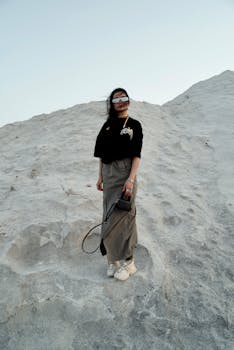 A woman in sunglasses stands on rocky terrain, evoking adventure and style.