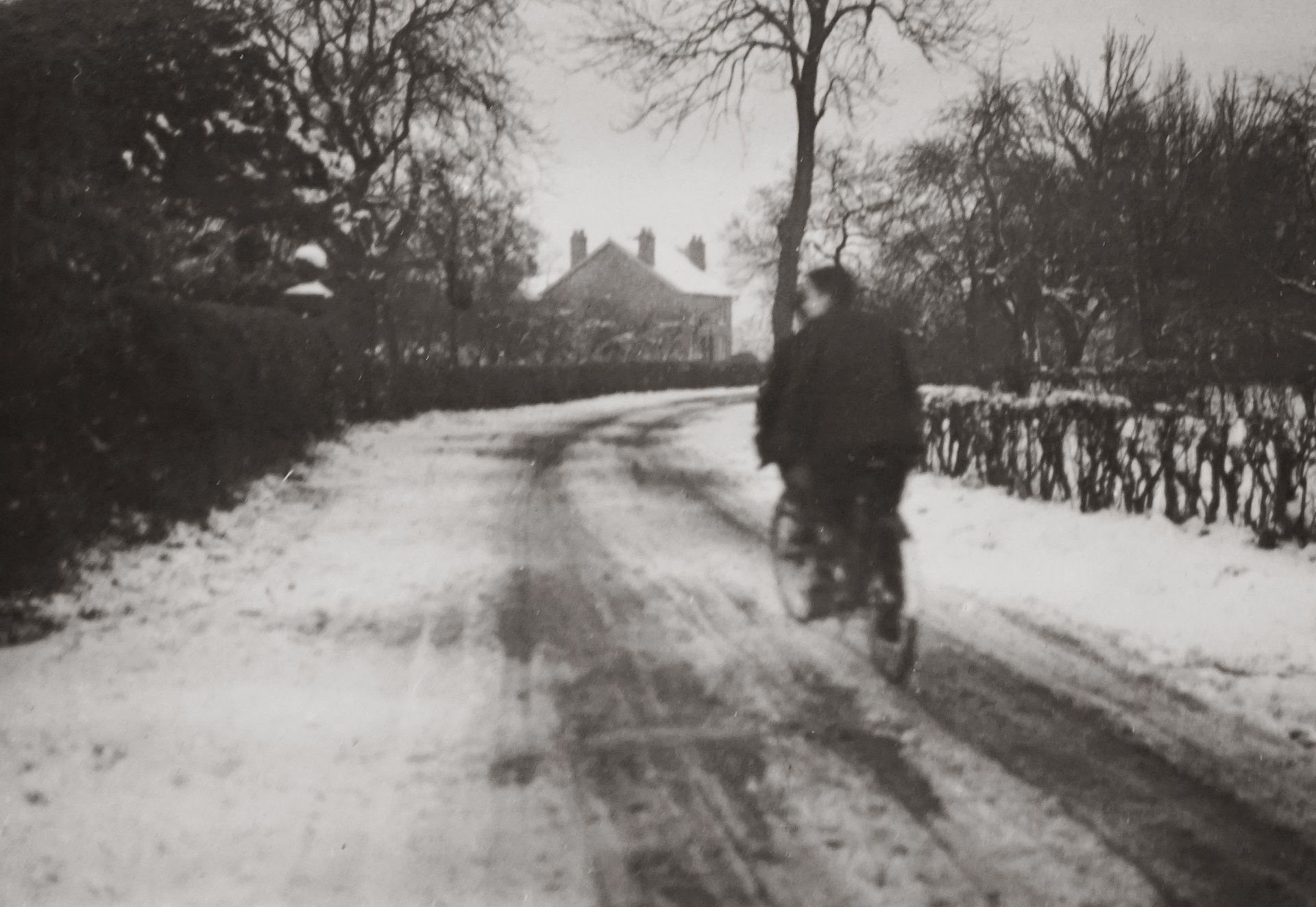 A cyclist rides on a snow-covered road capturing a vintage winter scene.