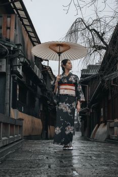 Woman in kimono with umbrella walking through traditional Kyoto street on a rainy day.