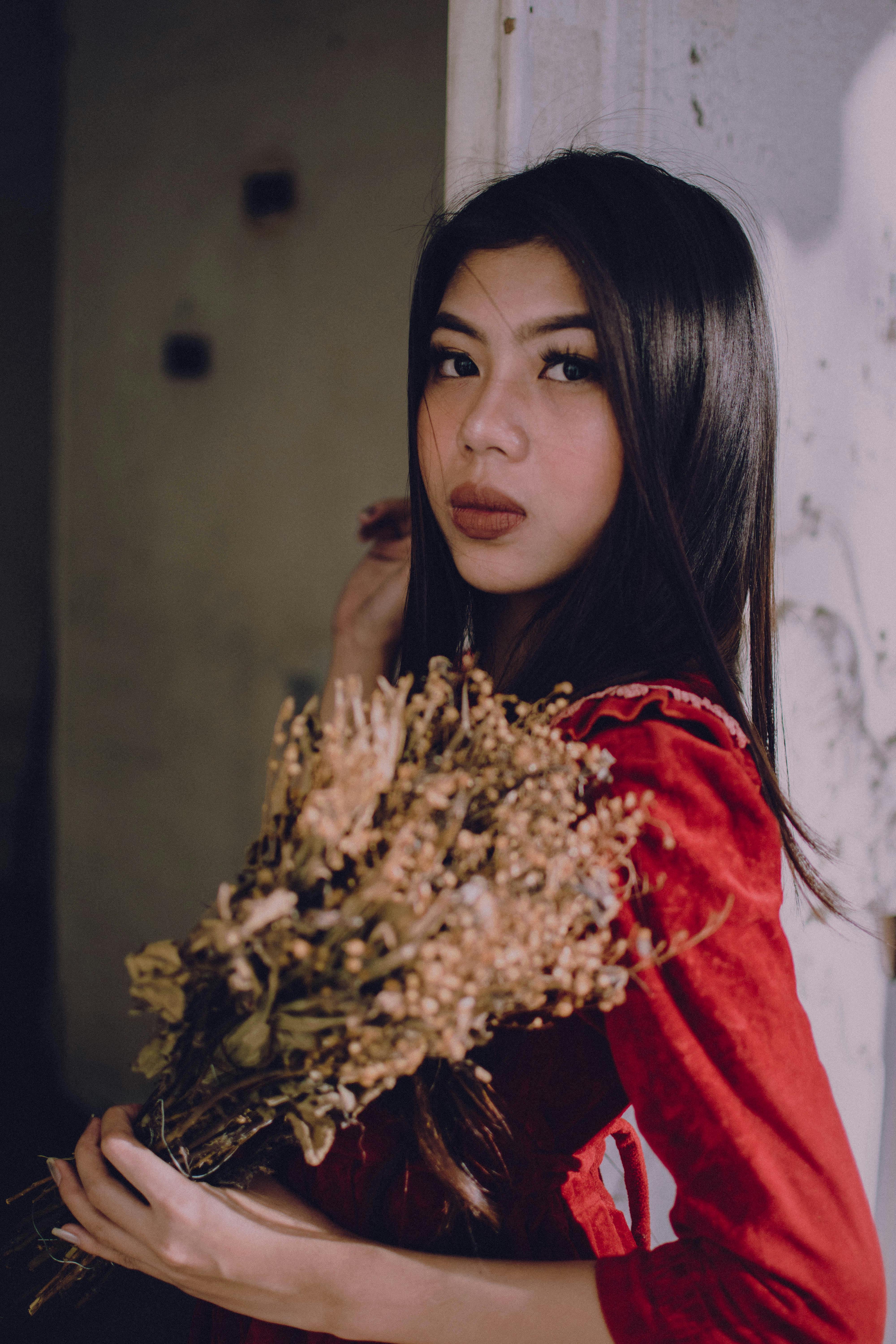 Portrait of a stylish woman in red holding a dried floral bouquet indoors.