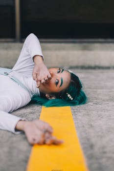 Fashionable woman with blue hair posing creatively on pavement outdoors.