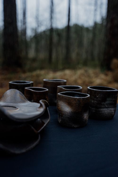 Free Handcrafted pottery cups and plates displayed outdoors in a serene forest setting. Stock Photo