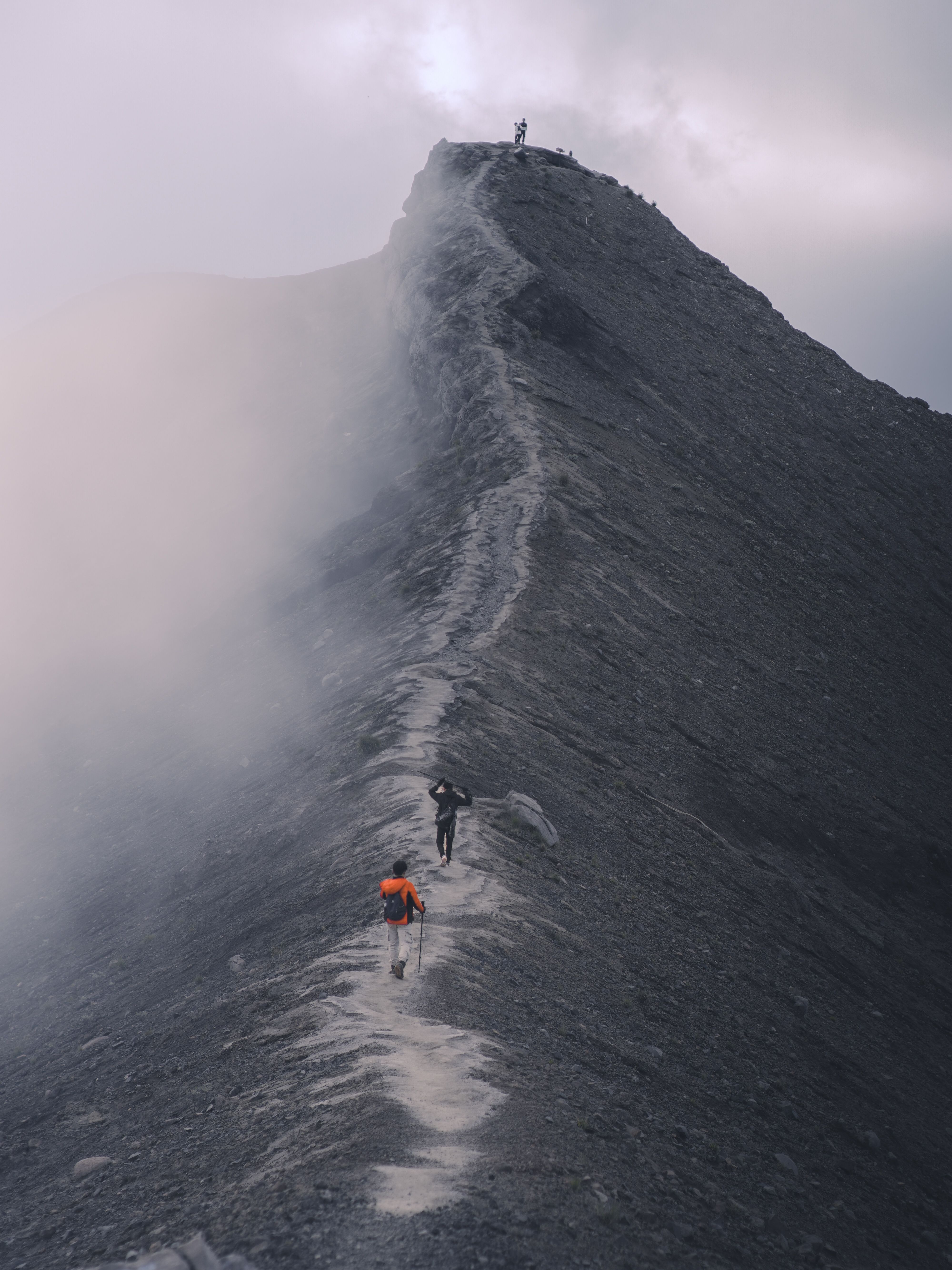 Hikers traverse a dramatic mist-covered mountain ridge, capturing the essence of adventure.
