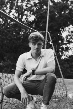 Black and white portrait of a young man posing outdoors by a net.