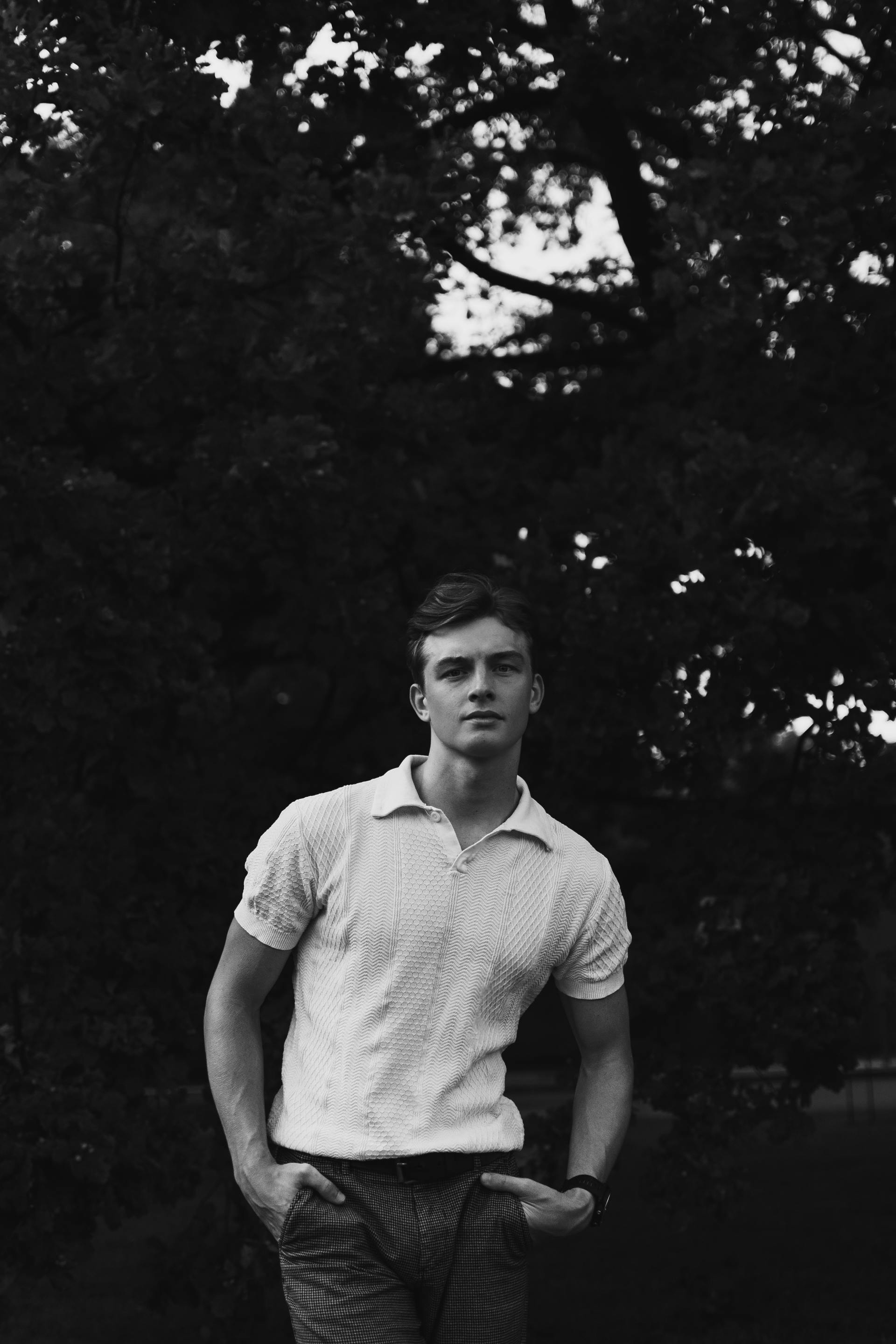 Stylish black and white outdoor portrait of a casual male model standing with hands in pockets.