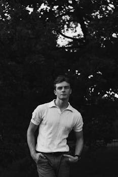 Stylish black and white outdoor portrait of a casual male model standing with hands in pockets.