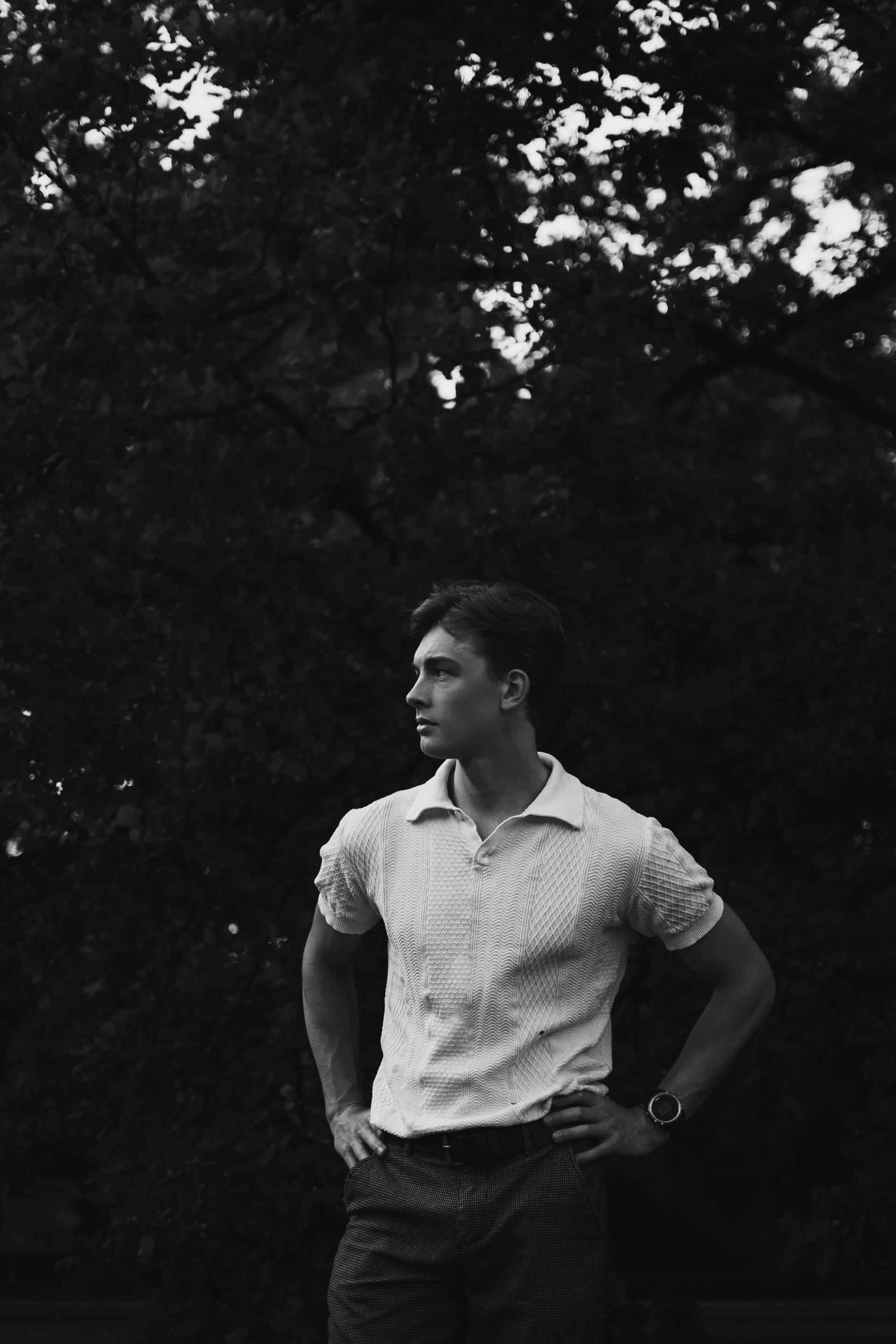 Striking black and white portrait of a man posing outdoors in casual attire.