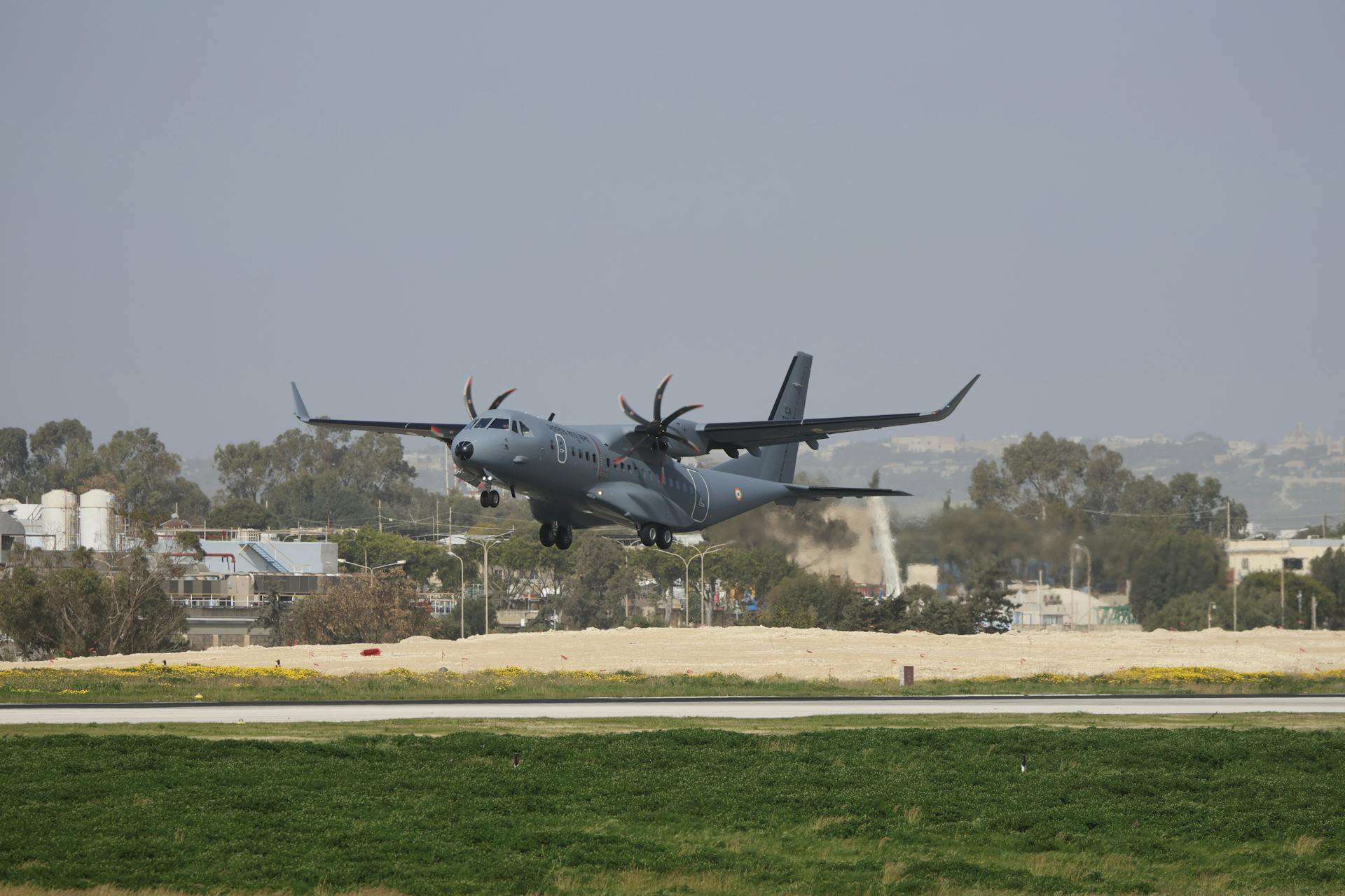 Military transport plane in final approach landing at an airport runway on a clear day.