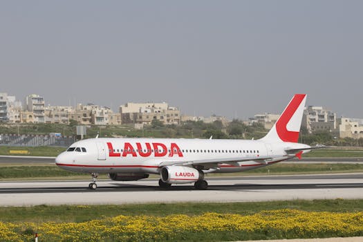 Lauda Airbus A320 aircraft taxiing on runway at an airport with cityscape backdrop.