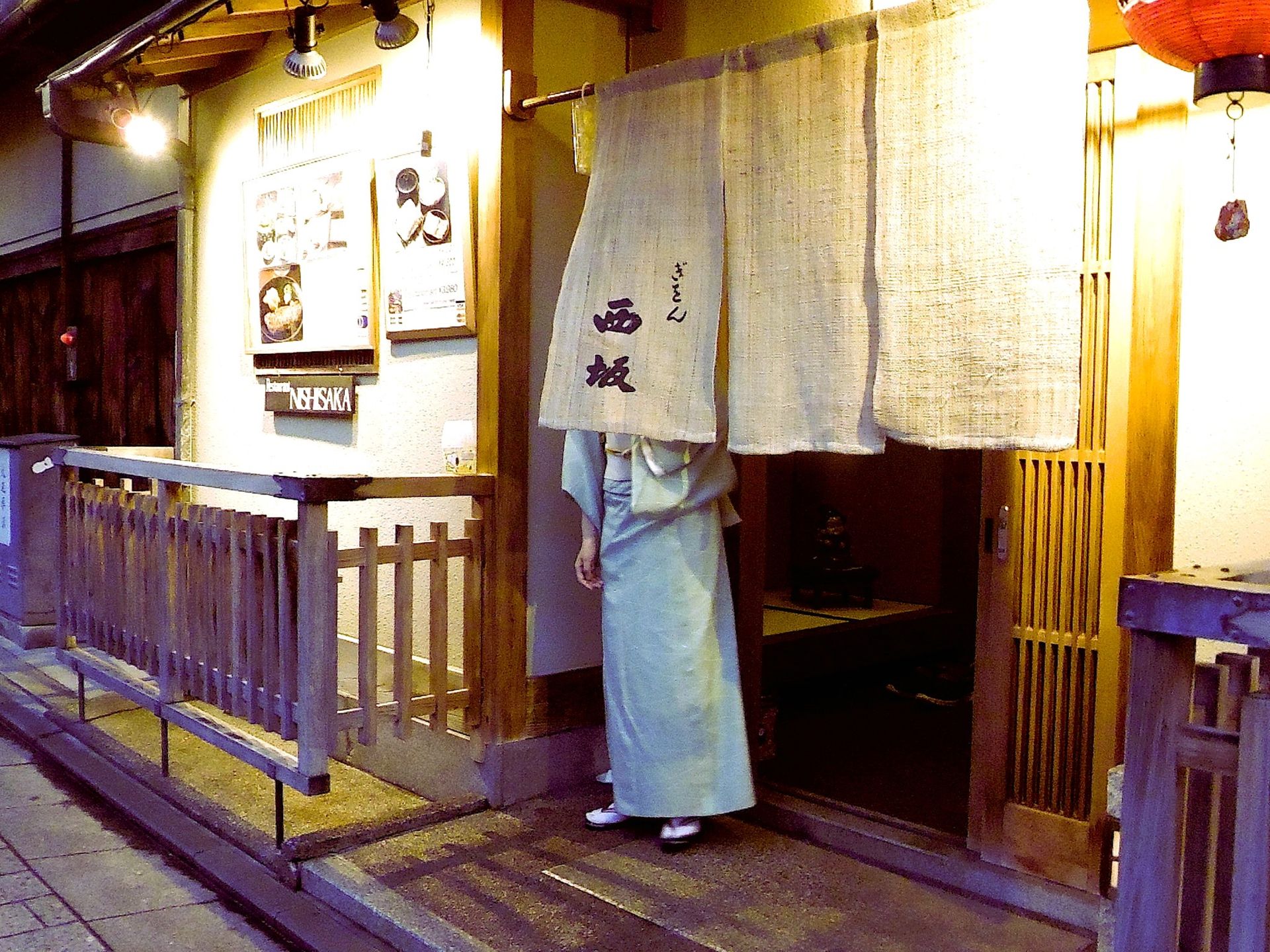 A person in traditional attire stands at a Japanese restaurant entrance with noren curtains.