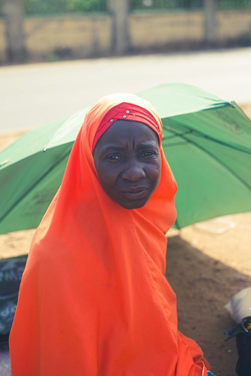 Free A woman wearing a bright orange hijab sitting outdoors with a green umbrella. Stock Photo