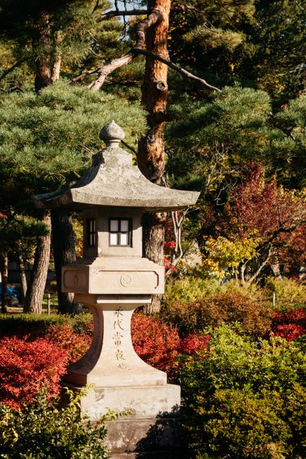 Tranquil Japanese garden landscape with stone lantern, autumn foliage, and pine trees.