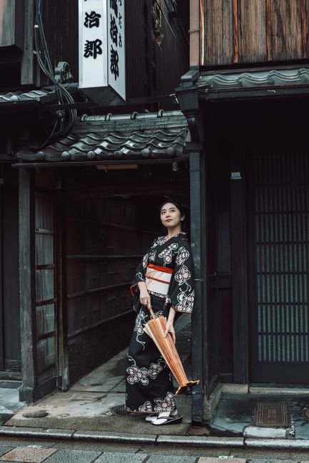 A woman in a kimono stands in a traditional Kyoto alley, capturing the essence of Japanese culture.