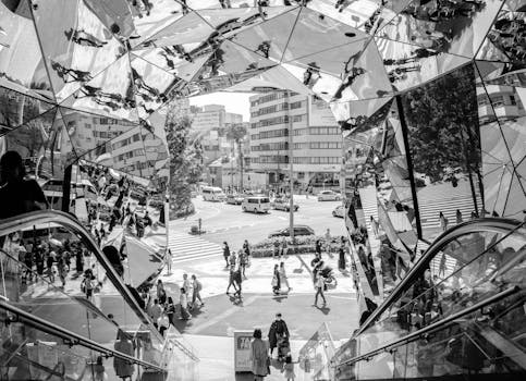 Black and white photo capturing city reflections and pedestrians in a mirrored tunnel.