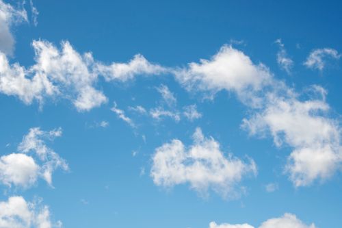 Free A serene daytime view of fluffy white clouds against a clear blue sky. Stock Photo