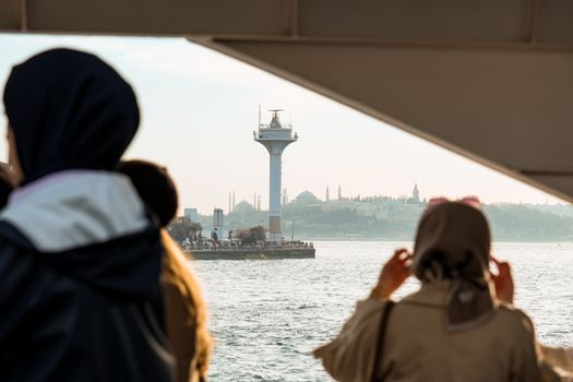 View of Istanbul's skyline and Bosphorus from a ferry with passengers in the foreground, capturing urban and historical vibes.