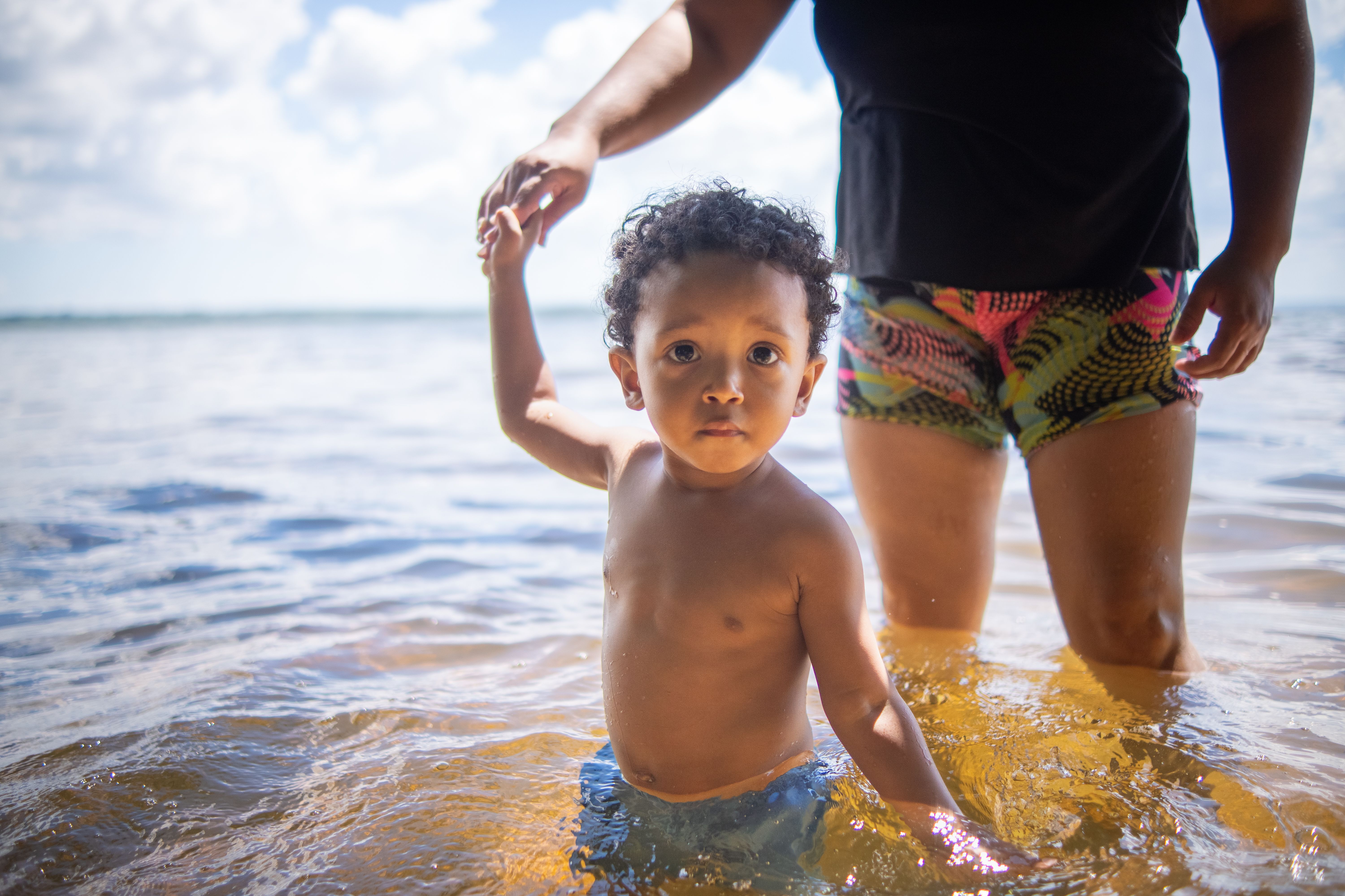 Un enfant heureux jouant dans l'eau sur une plage ensoleillée avec un gardien.