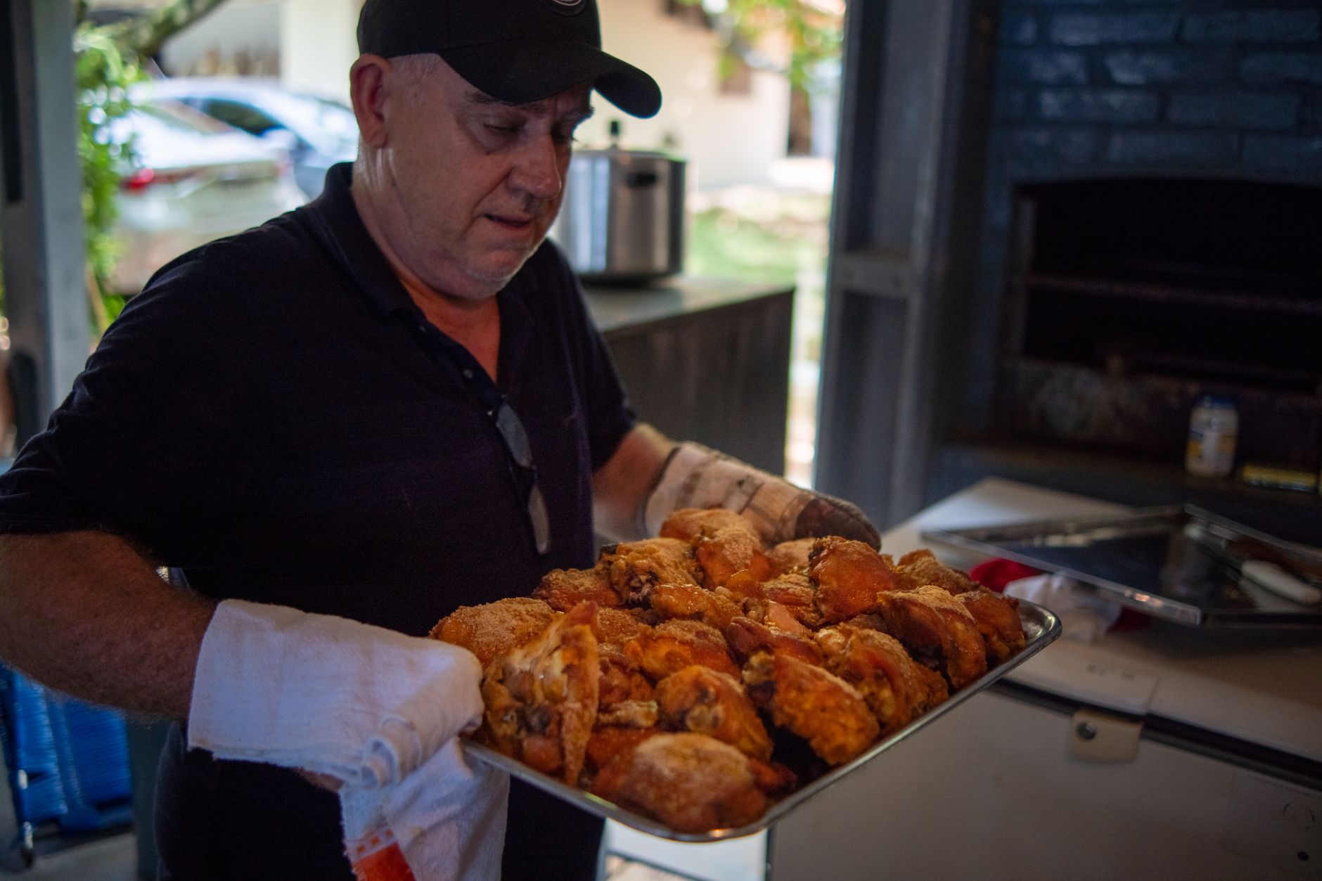 A man carrying a tray of roasted chicken in a rustic kitchen setting.