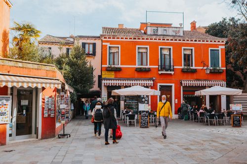 Free Colorful street in Burano, Italy with lively outdoor cafes and pedestrians. Stock Photo