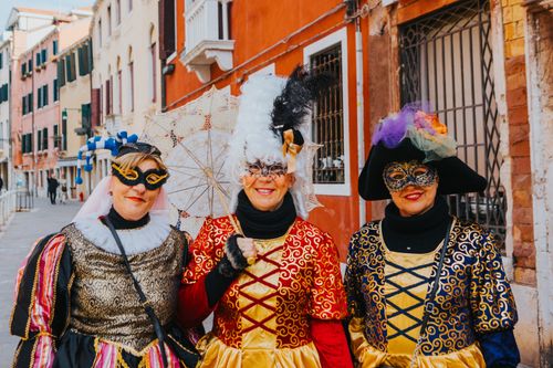 Free Three women in vibrant carnival costumes with masks, enjoying a sunny day in Venice. Stock Photo