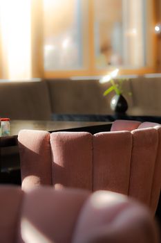Sunlit corner of a cozy cafe featuring a plush pink chair, a table, and a vase with a single flower.