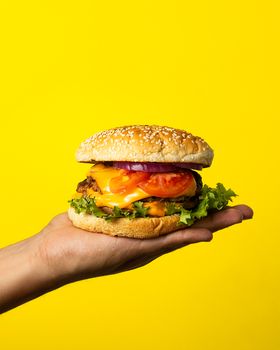 Juicy cheeseburger with fresh toppings on a vibrant yellow background.