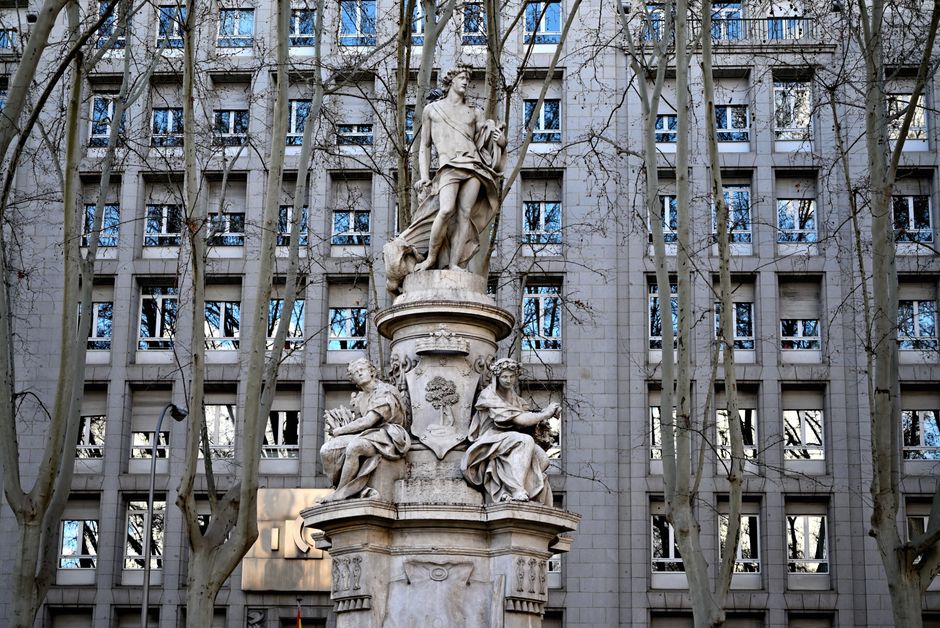 Estatua rodeada de árboles desnudos frente a un edificio histórico en Madrid, España.