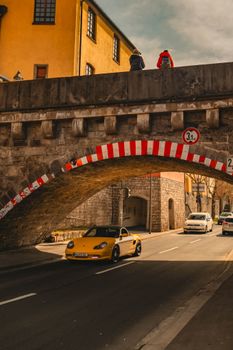 A yellow car drives under a historic stone bridge in a picturesque urban setting.