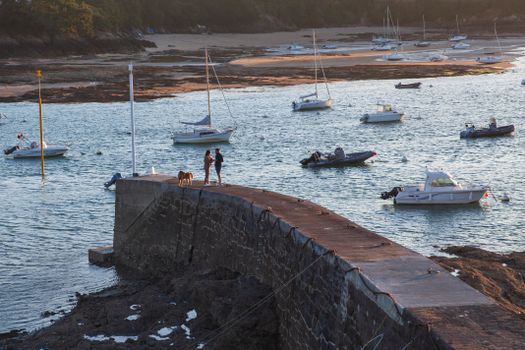 Scenic view of a couple with a dog on a stone pier in Brittany with moored boats.