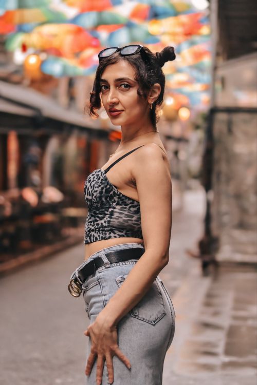 Free Confident woman in trendy attire poses under vibrant umbrellas in charming urban setting. Stock Photo
