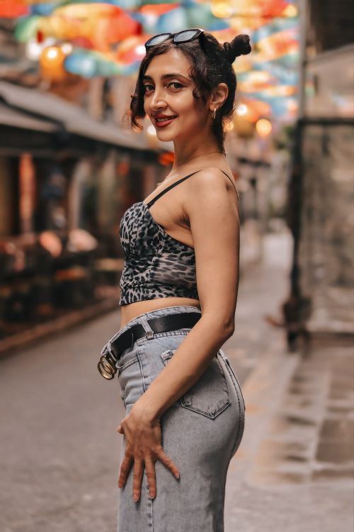 Free Fashionable woman poses on a vibrant street with colorful hanging lanterns, showcasing casual style. Stock Photo