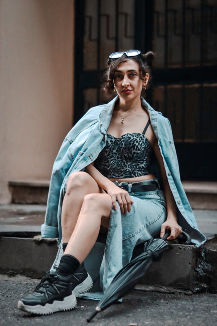 Stylish woman in denim and leopard print top sits on steps with umbrella.