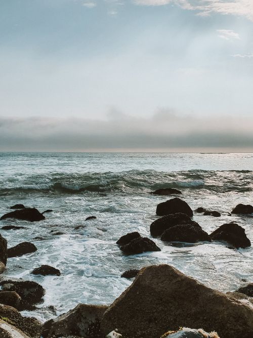 Free Tranquil view of rocky shoreline with gentle waves at sunrise, ideal for relaxation themes. Stock Photo