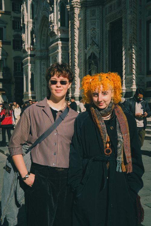 Free Two trendy individuals stand confidently in front of a historic cathedral, showcasing their unique style. Stock Photo