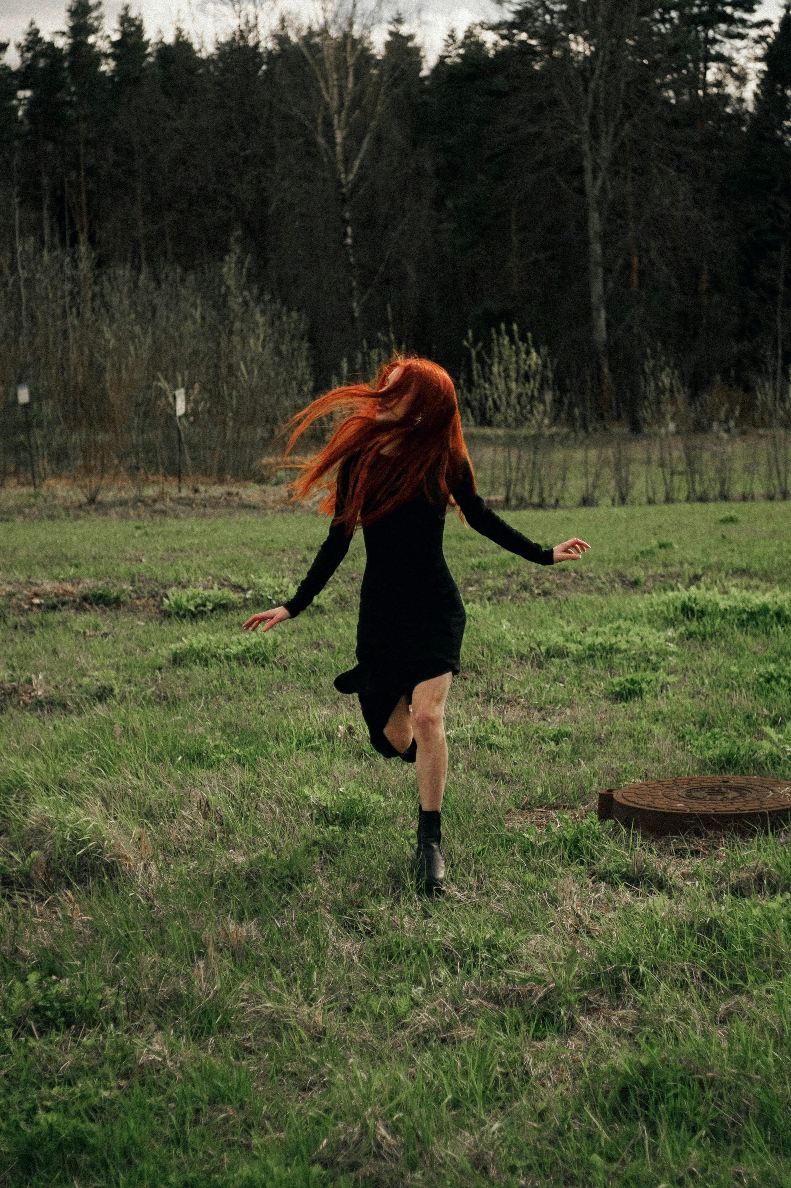 Gratis En kvinne med langt rødt hår som løper gjennom en frodig eng, og viser frihet i naturen. Arkivbilde