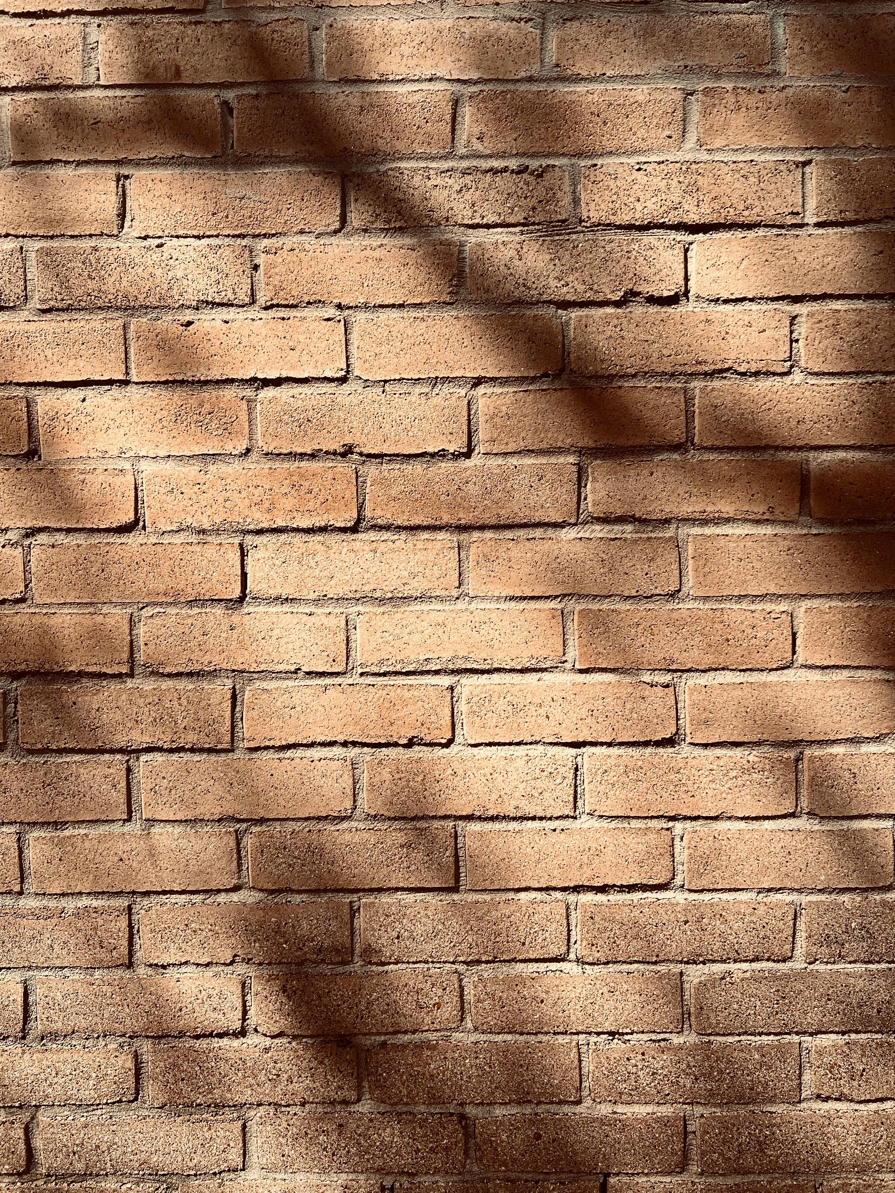 gratis Zonovergoten oranje bakstenen muur met schaduwen, perfect voor achtergronden en architectuurthema's. Stockfoto