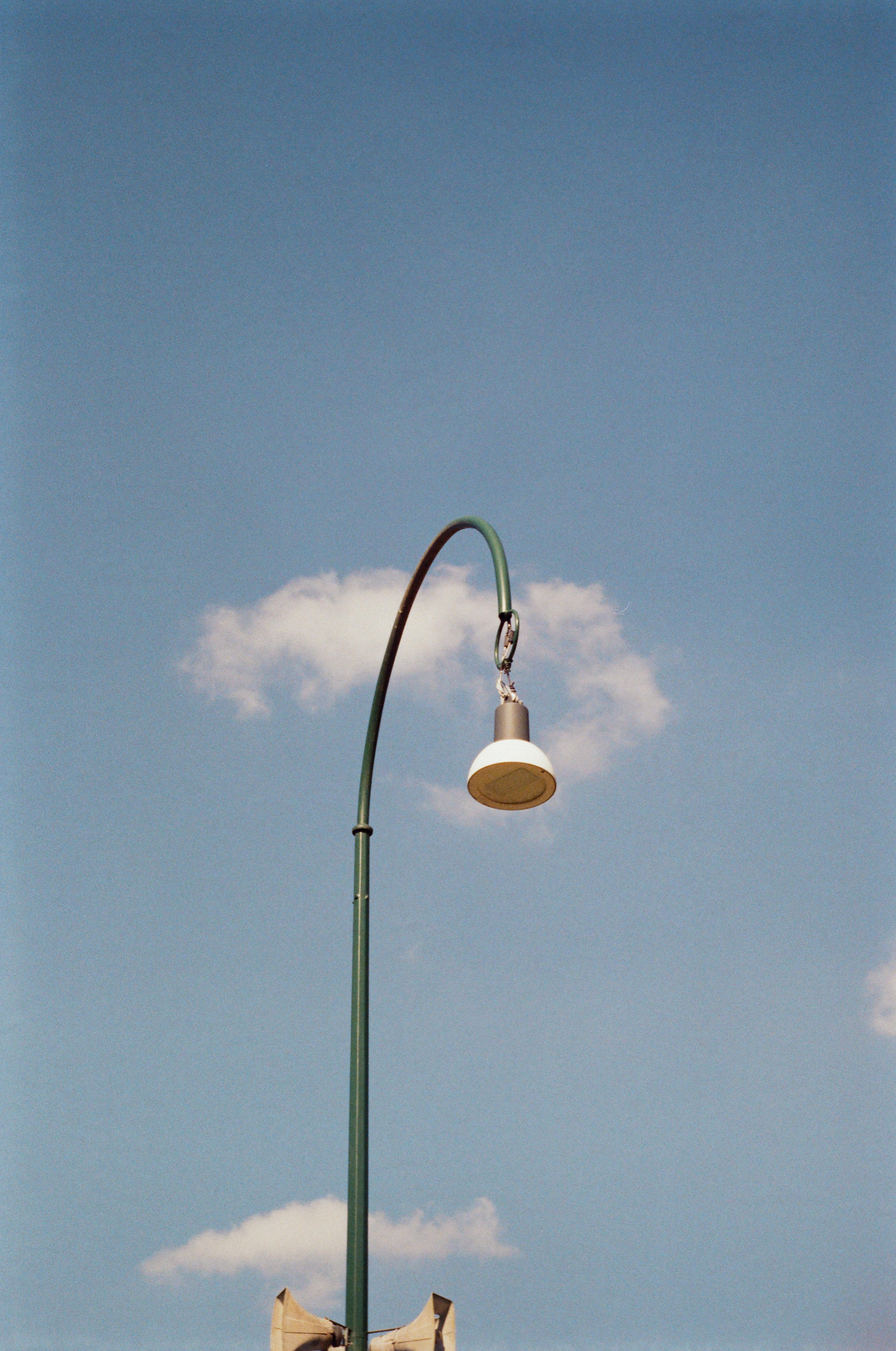 A street lamp set against a bright blue sky with fluffy clouds, creating a minimalistic scene.