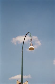 A street lamp set against a bright blue sky with fluffy clouds, creating a minimalistic scene.
