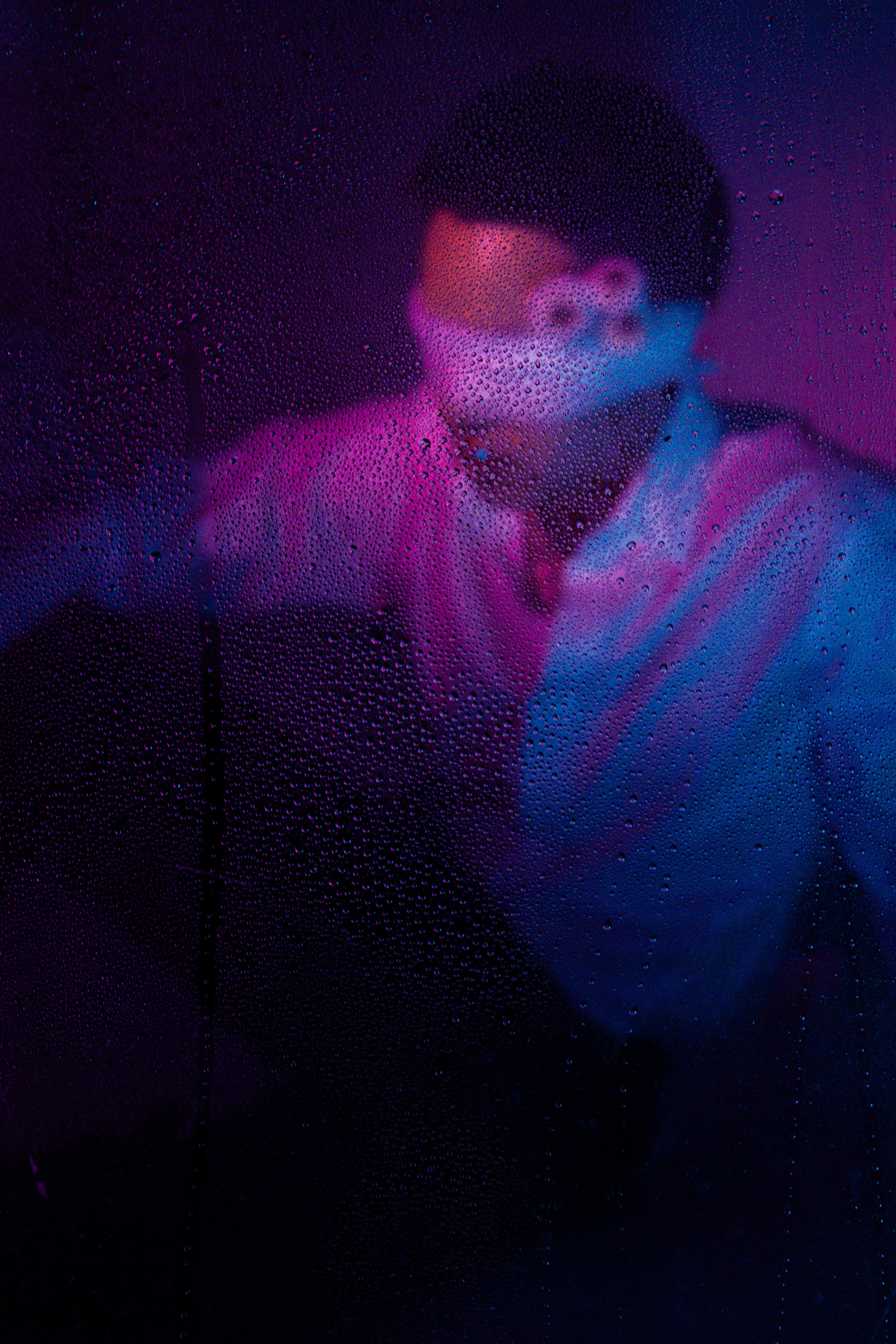 Abstract portrait of a male model in vibrant purple and blue lighting, with water droplets adding a creative effect.