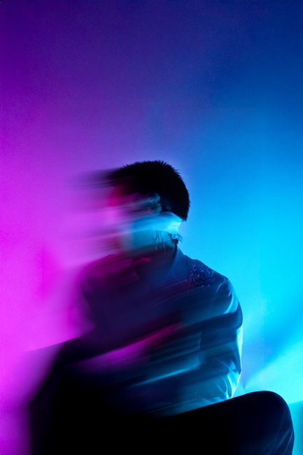Blurred portrait of a male model in purple and blue lighting, creating an abstract effect.