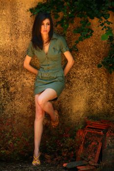 Woman in green dress posing against textured wall with foliage.