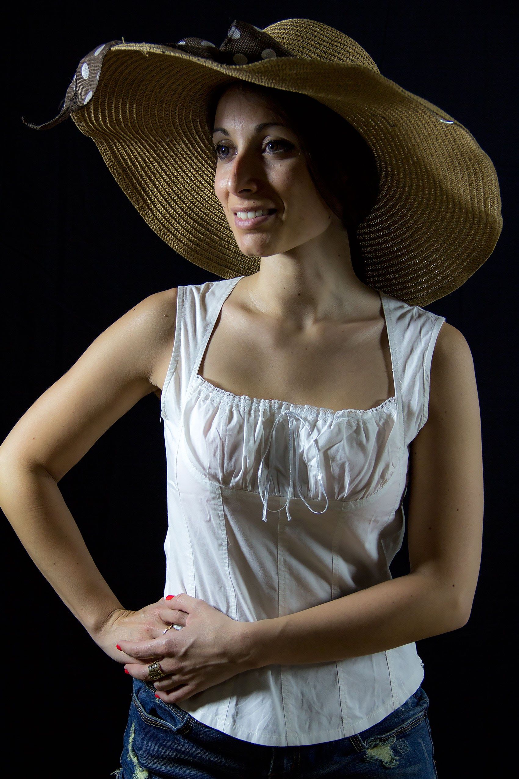 Portrait of a smiling woman in a wide-brimmed sun hat and white top against a dark background.