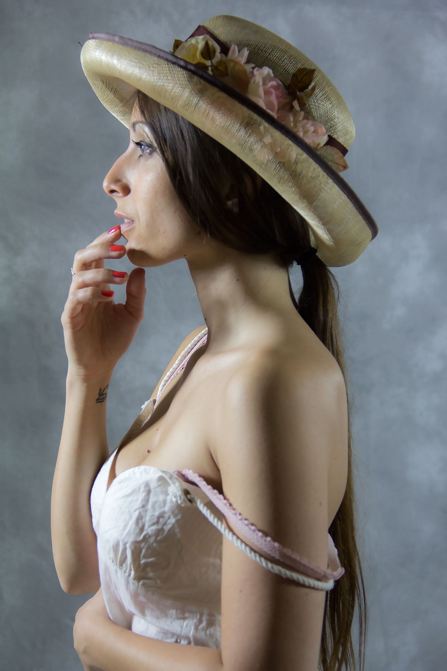 A thoughtful woman in a vintage hat and strapless dress against a textured background.