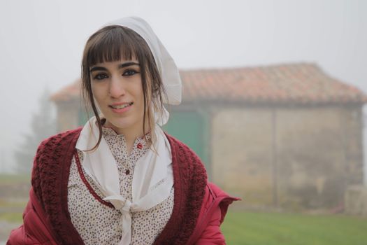 Portrait of a young woman with a traditional headscarf in a foggy rural setting.