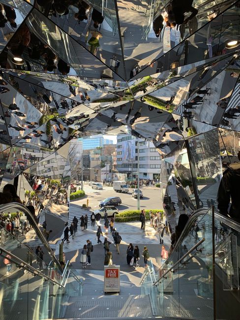 View of bustling city street through reflective glass kaleidoscope entry in Tokyo.