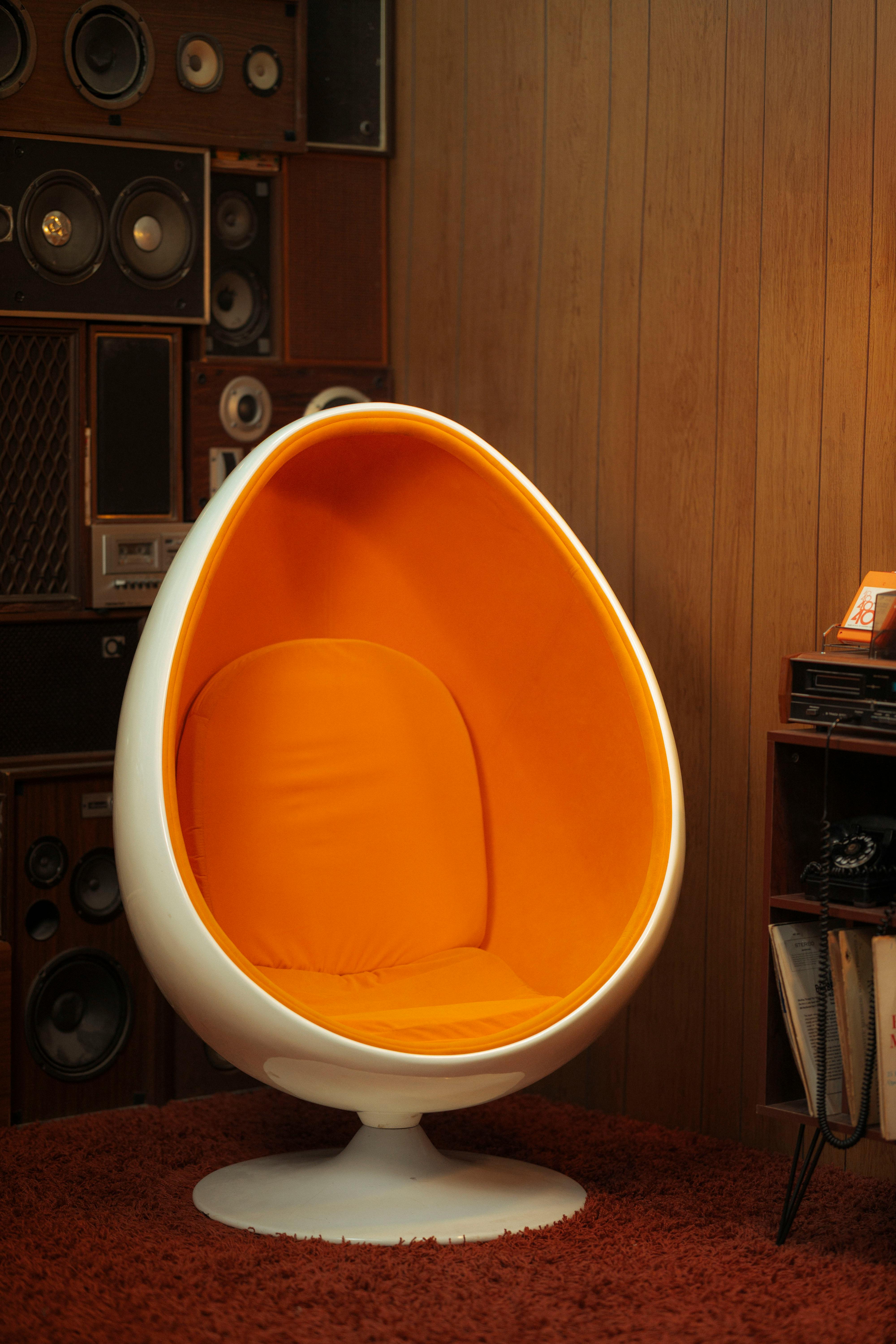 A stylish retro egg chair in an orange hue set against a vintage audio system.