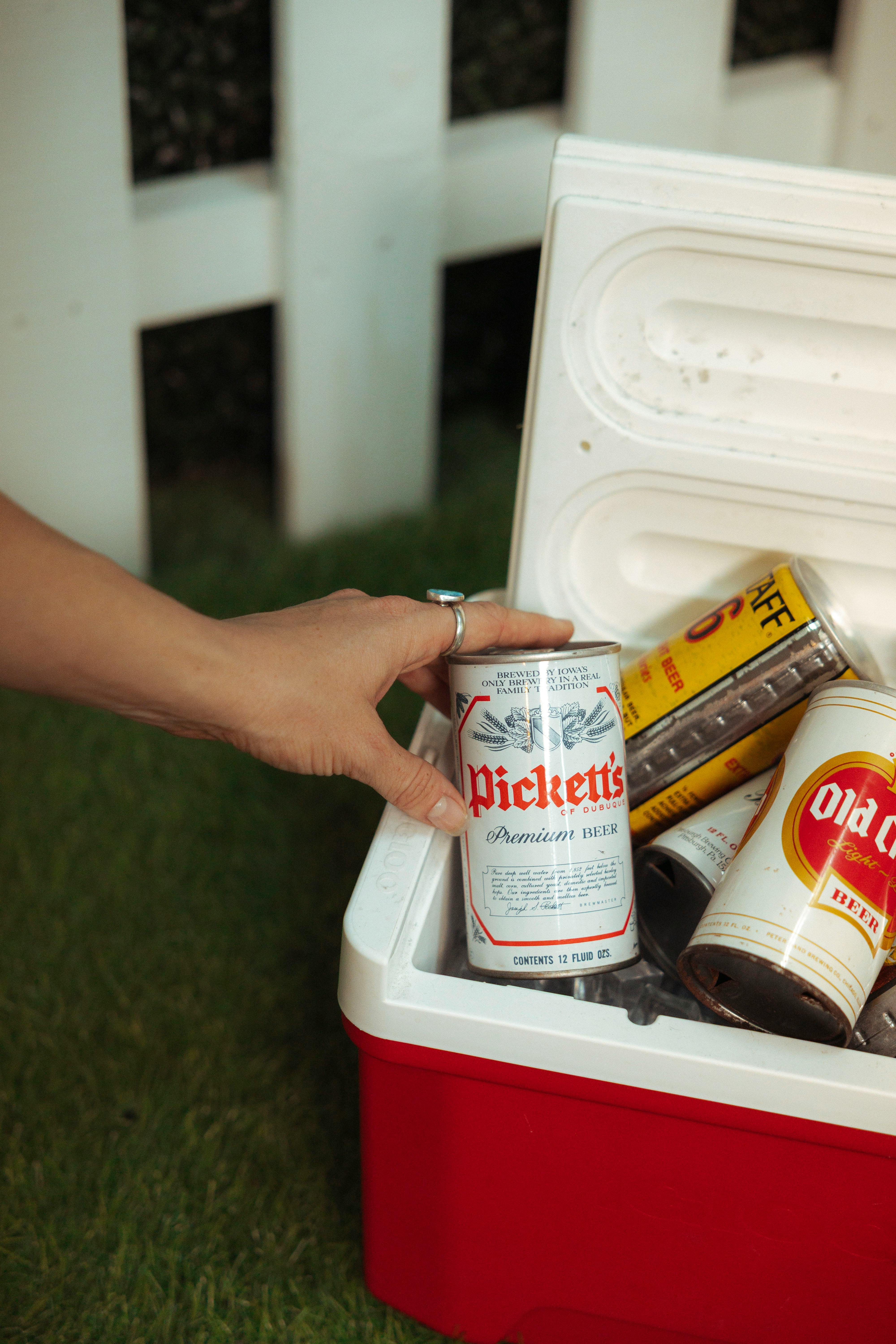 A relaxed outdoor scene showing a hand reaching for a beer can in a cooler.