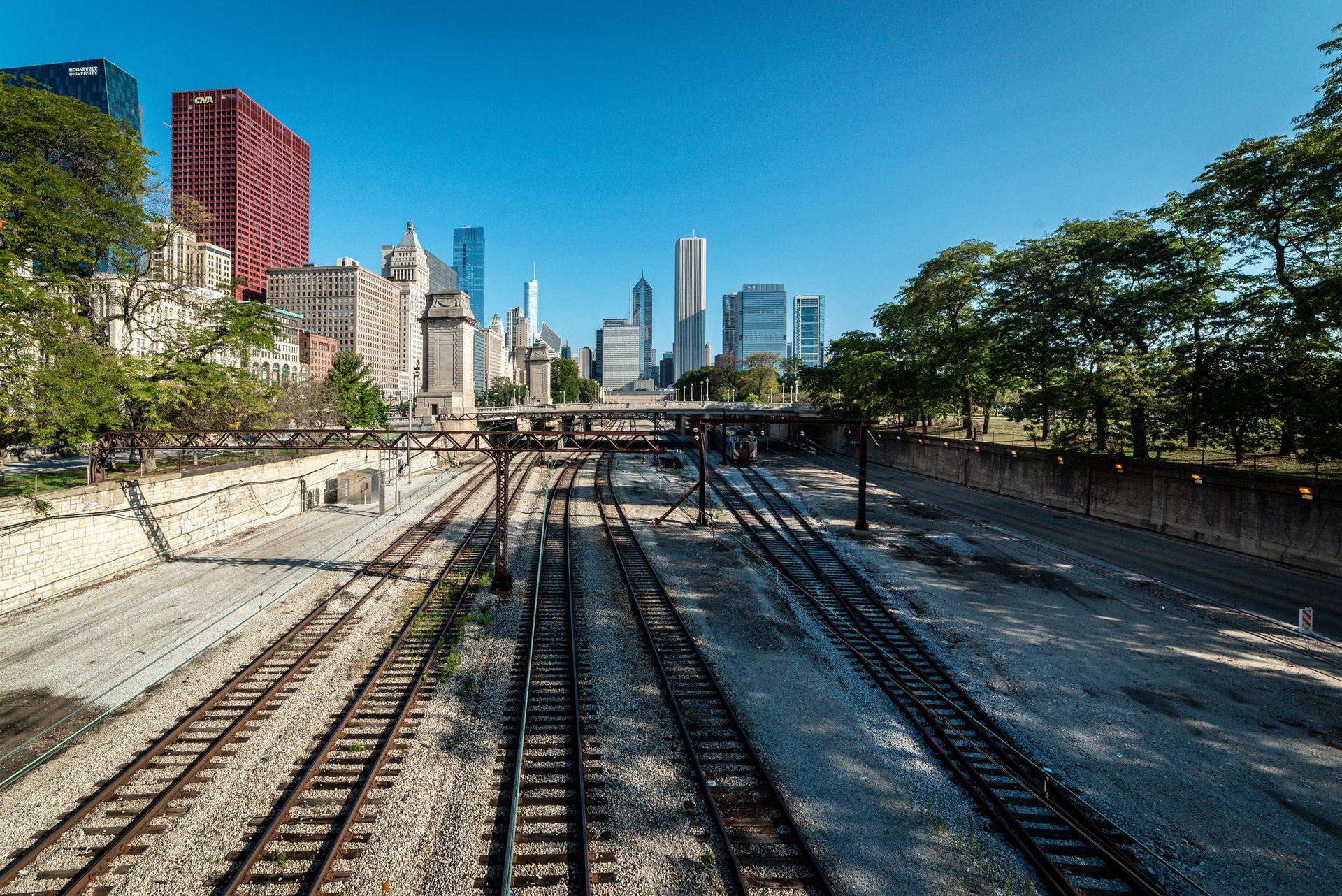 Chicago skyline viewed from the West Loop with railroad tracks, green trees, and blue sky