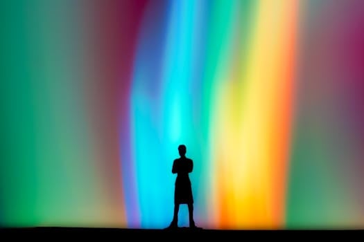 A lone silhouette of a person stands against a vibrant, rainbow-like abstract background.